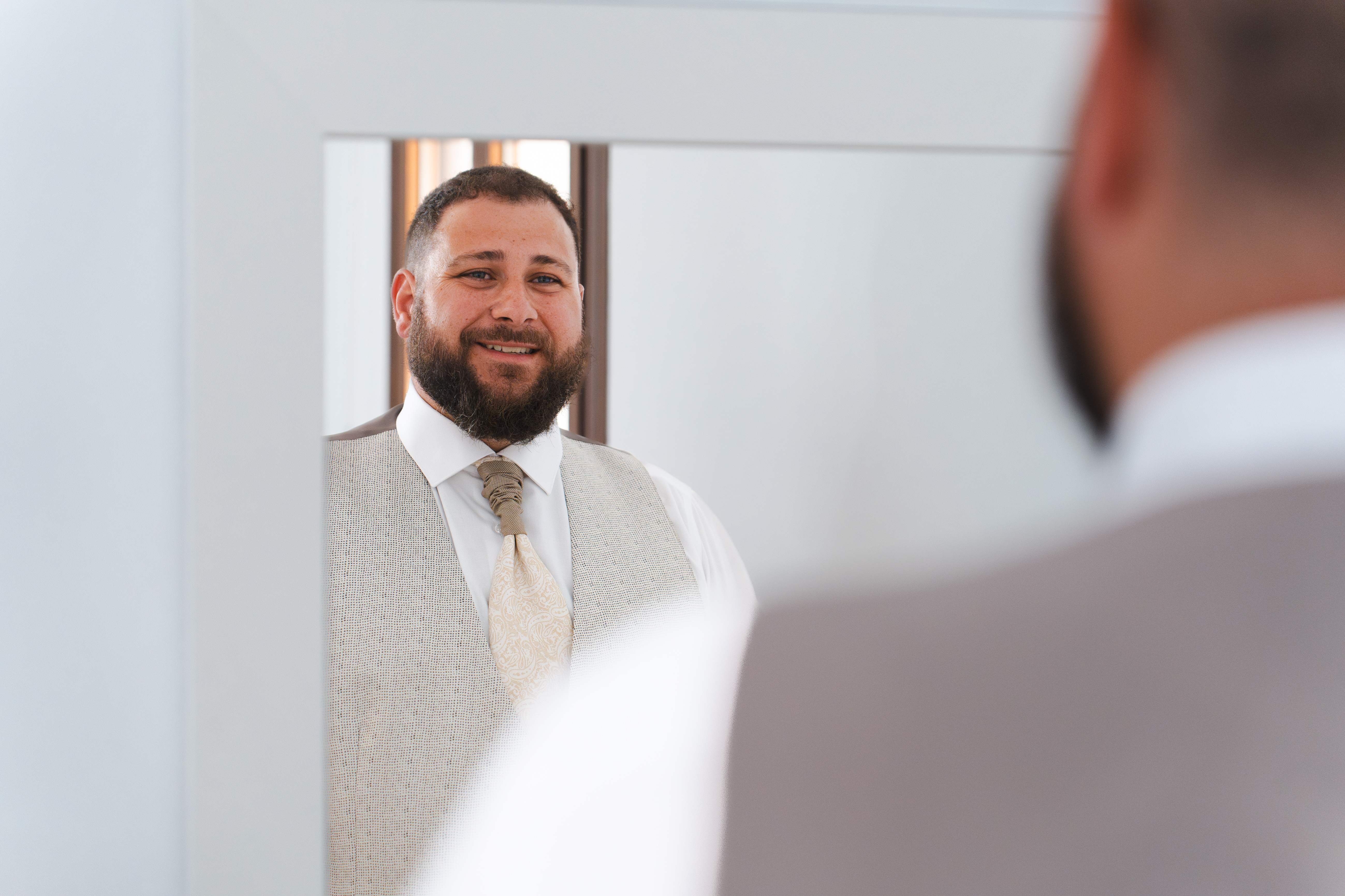 Novio sonriendo mientras se prepara frente al espejo antes de la boda