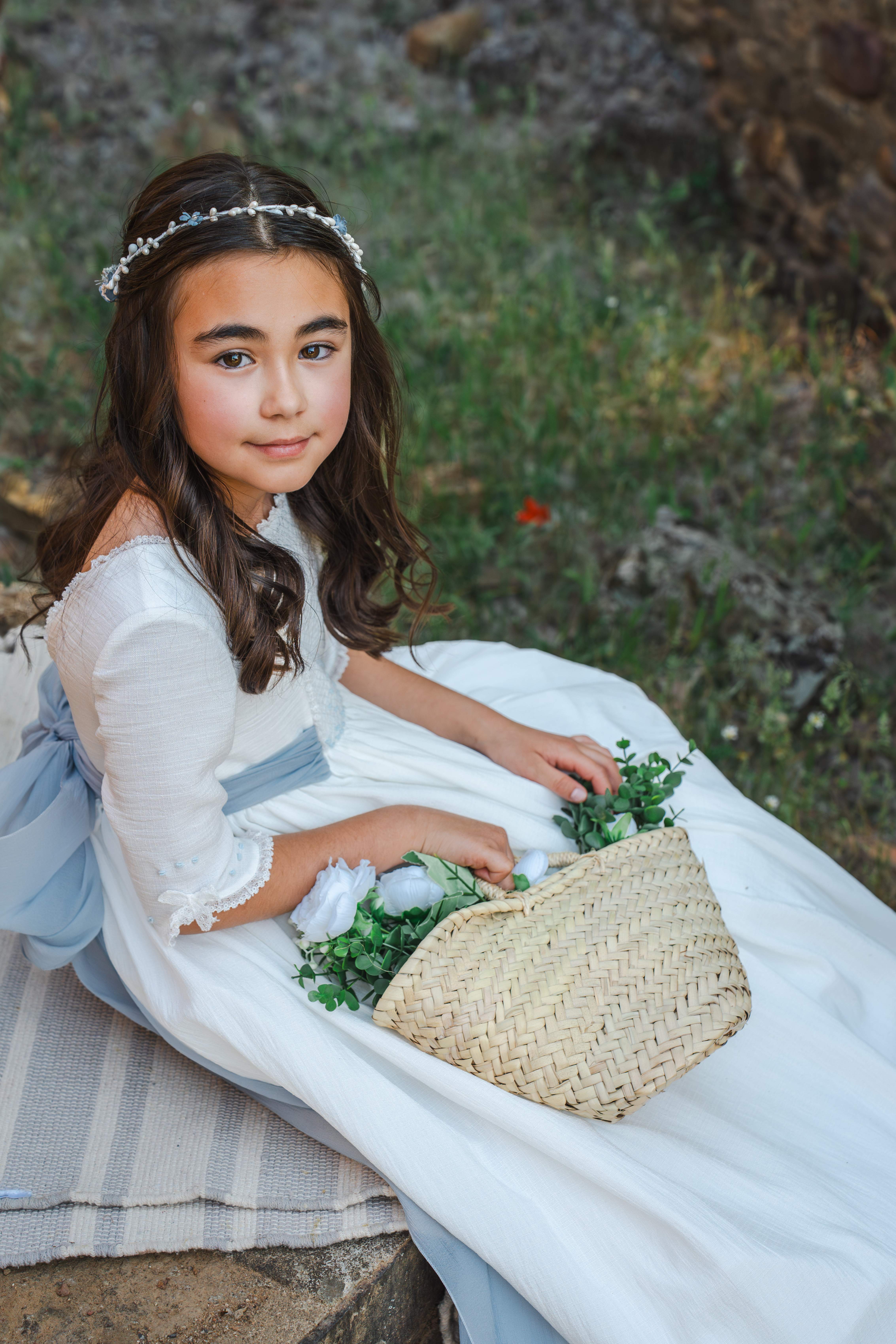 Retrato de una niña de comunión sentada junto a una cesta de flores
