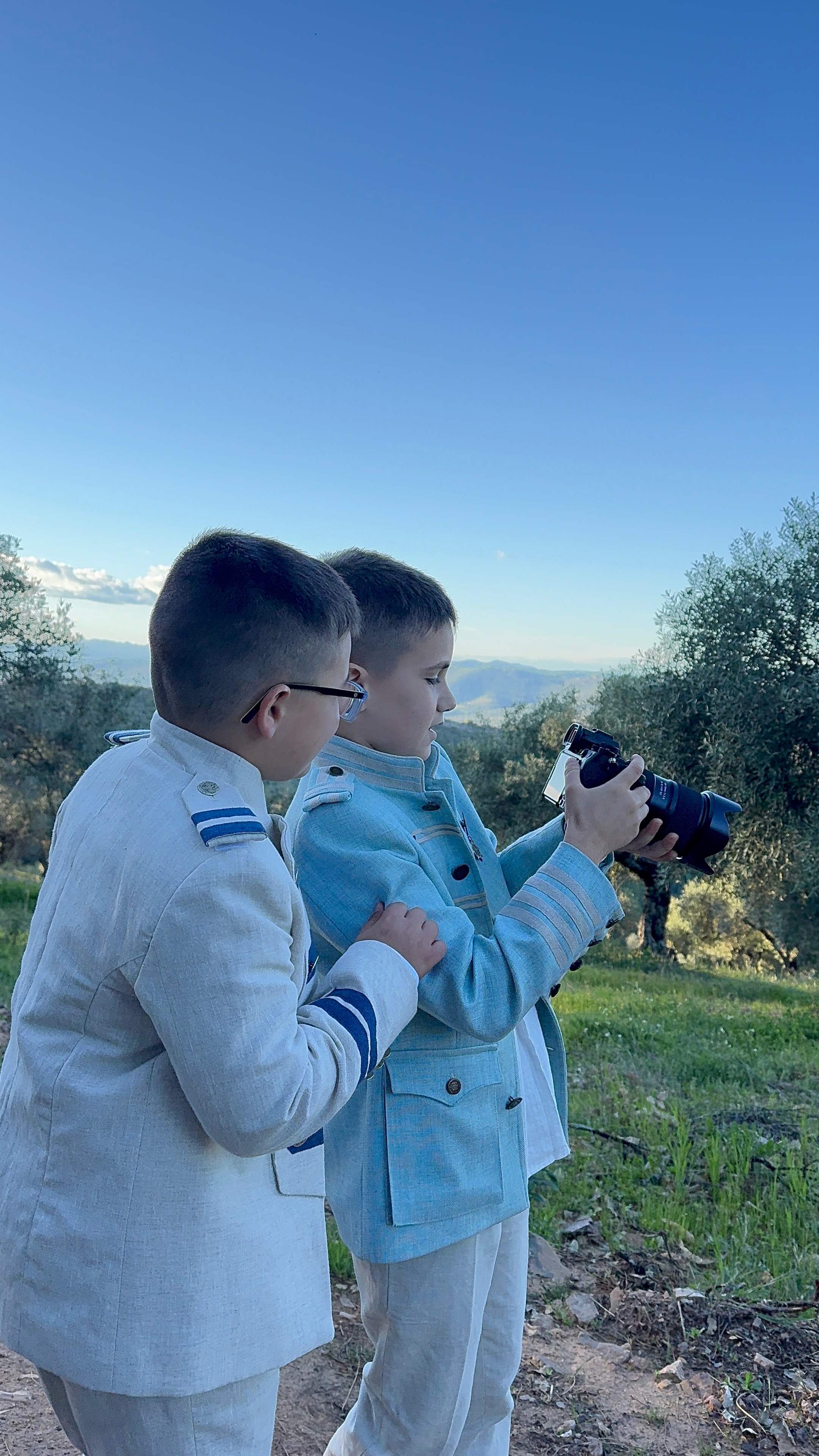 Dos niños vestidos de comunión revisando juntos una fotografía en la cámara