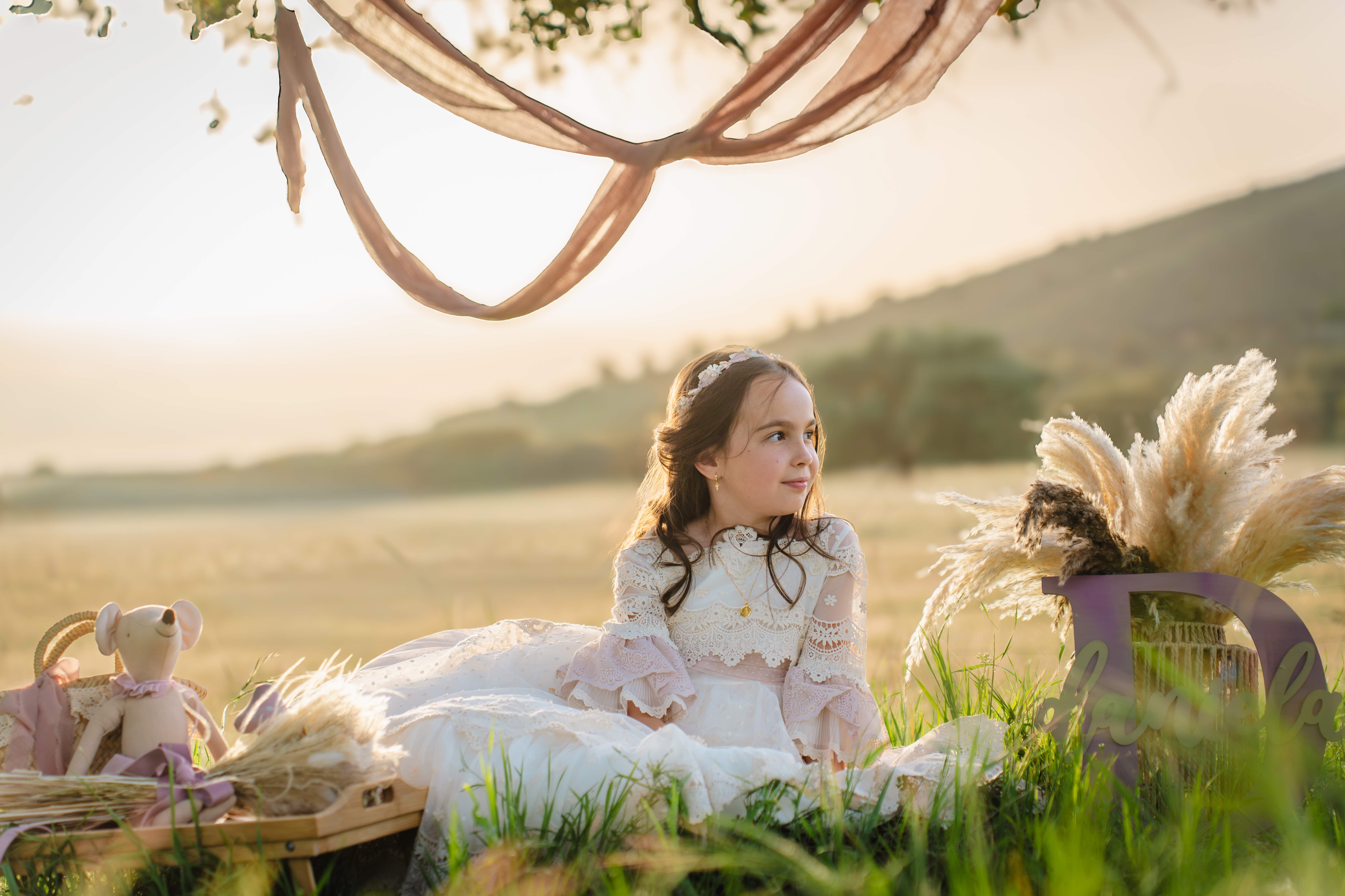 Niña de primera comunión sentada en el campo con luz dorada al atardecer